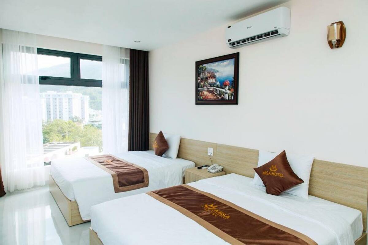 A hotel room with two beds, a large window, an air conditioning unit, and a painting on the wall.