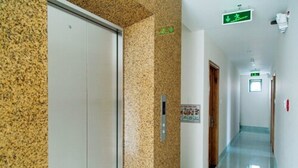 A hallway with a granite wall, a door, and a green exit sign. - Misa Hotel (Quy Nhon Nam)