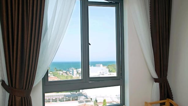 A room with a large window, curtains, and a wooden chair. - Misa Hotel (Quy Nhon Nam)