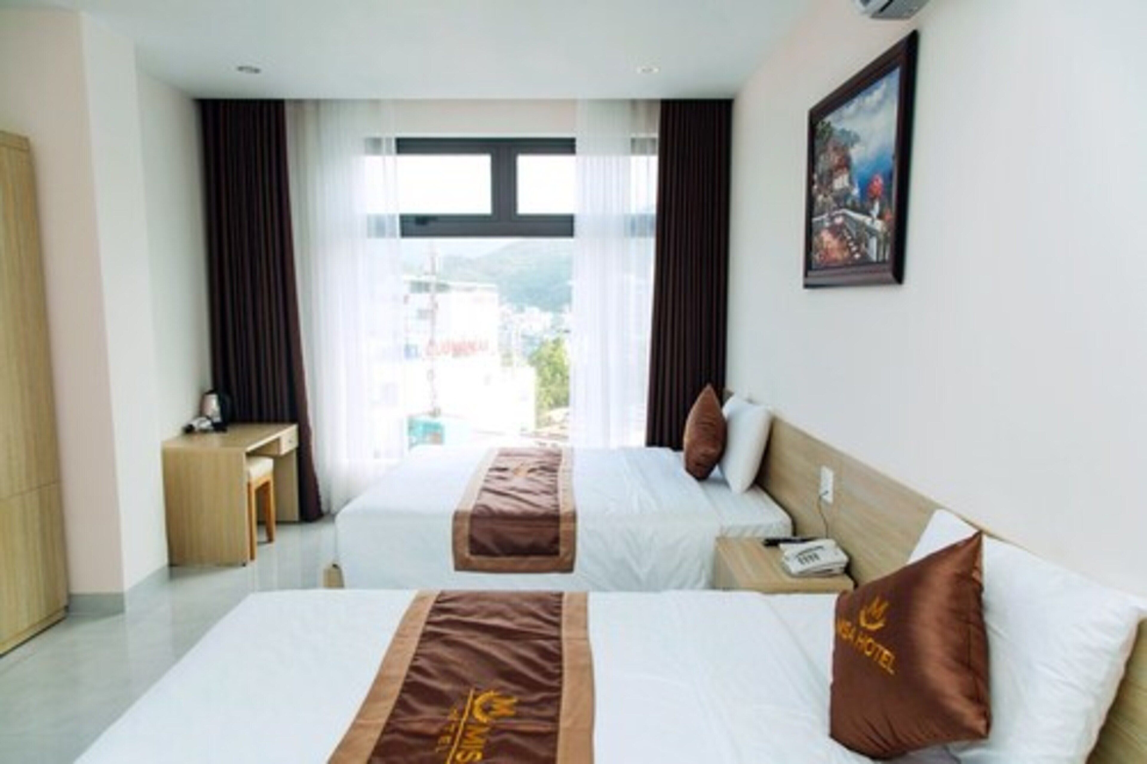 Habitación de hotel con dos camas, un escritorio y una ventana con vistas a edificios y montañas.