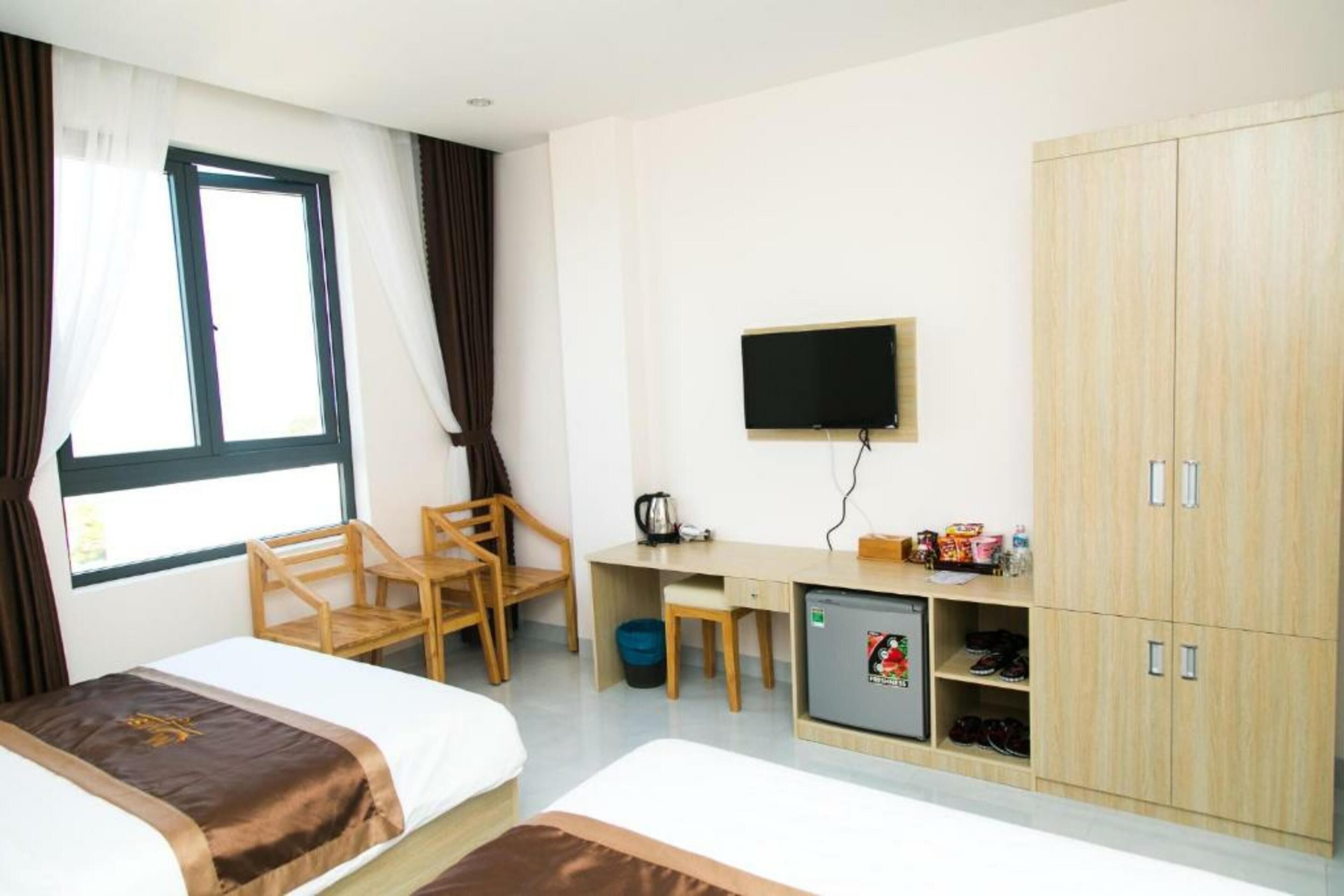 Habitación de hotel con dos camas, un escritorio con televisor, un armario y un refrigerador pequeño.