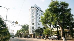 A multi-story hotel with a modern design, located on a street with trees and parked vehicles. - Misa Hotel (Quy Nhon Nam)