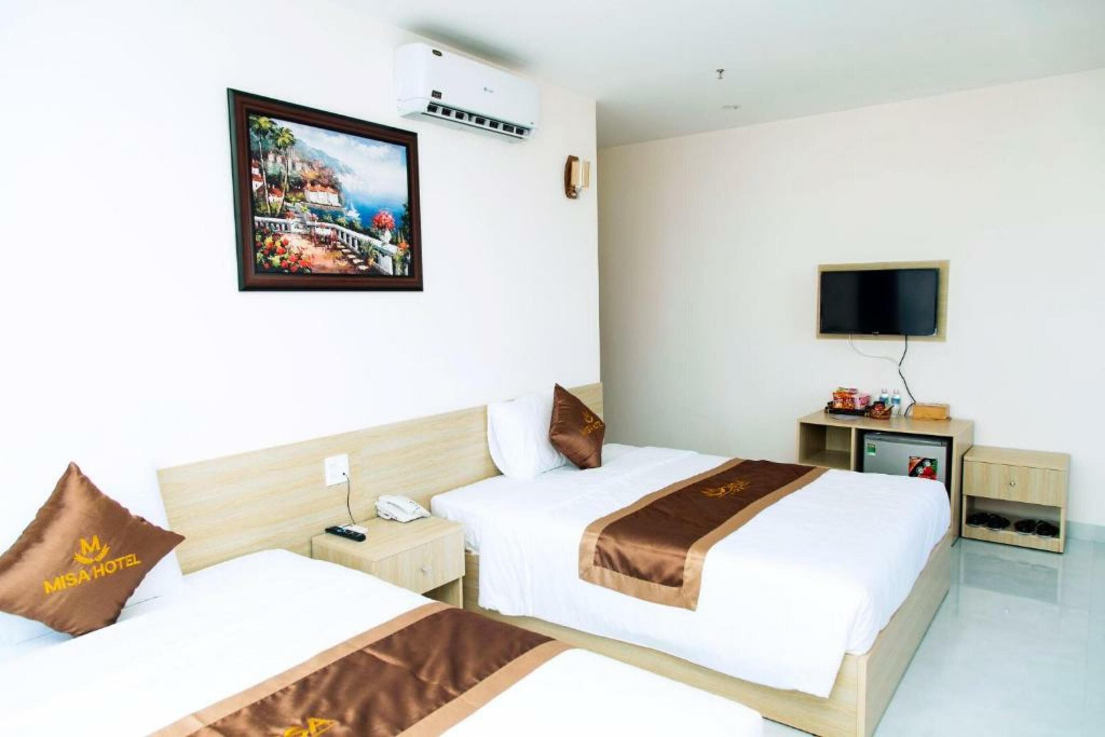 A hotel room with two beds, a TV, a desk, a phone, and a painting of a coastal scene.