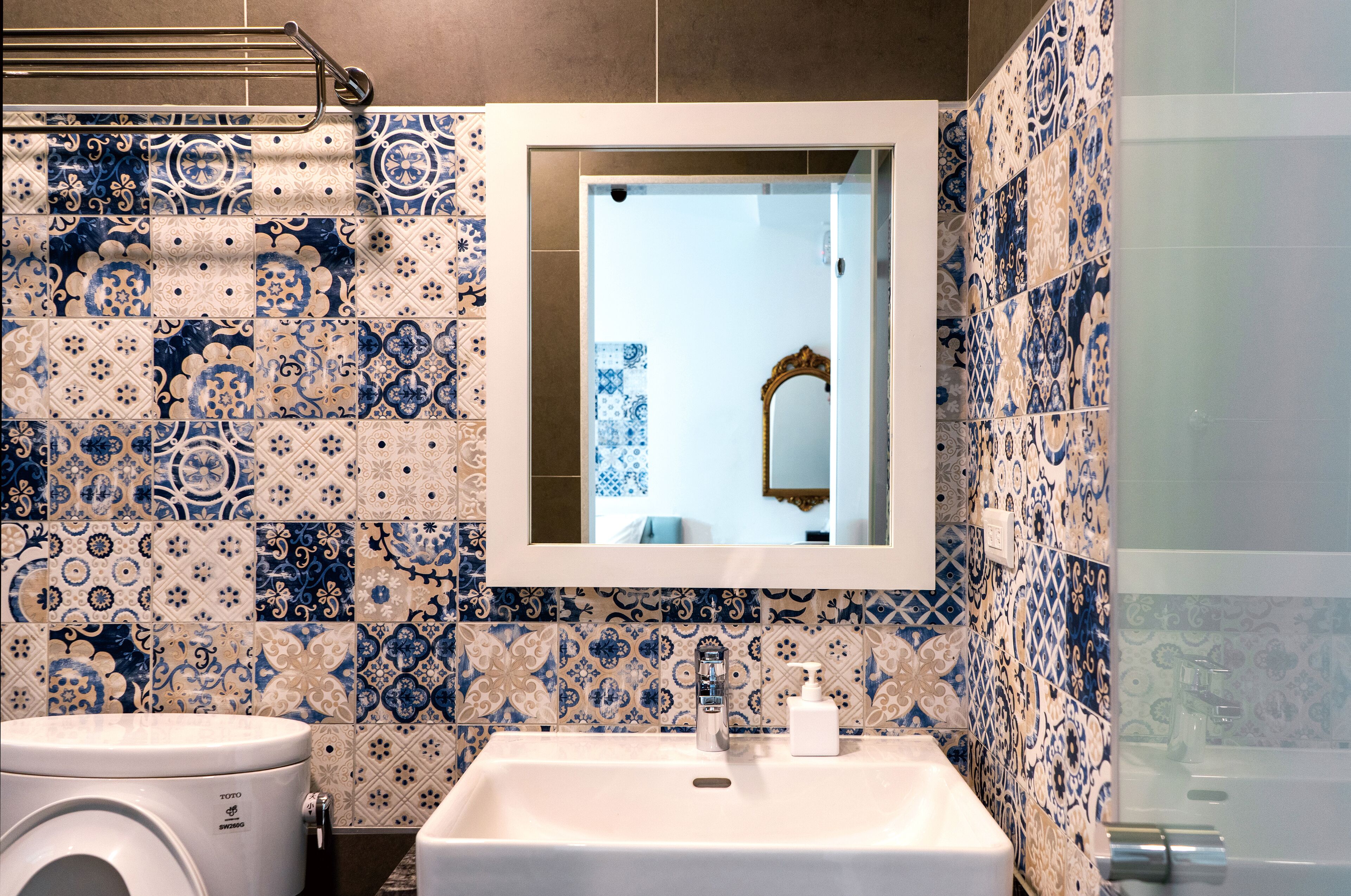 A bathroom with a sink, mirror, and patterned tiles.