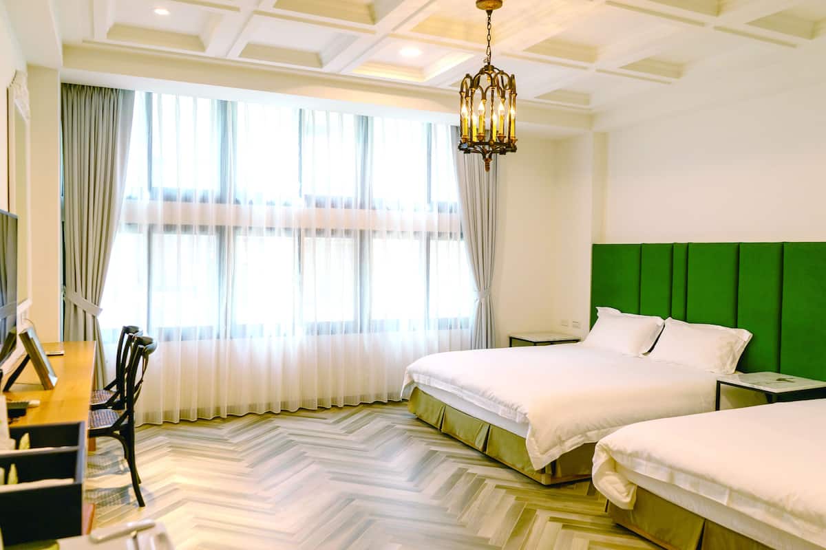 Ein Hotelzimmer mit zwei Betten, einem Esstisch mit Stühlen und einem großen Fenster mit Vorhängen.