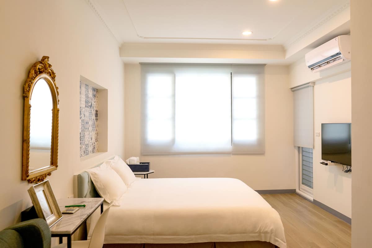 Ein Hotelzimmer mit einem großen Bett, einem Schreibtisch mit Stuhl, einem Fernseher und einem Fenster mit Jalousien.