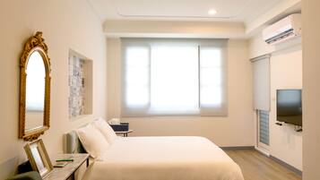 A hotel room with a large bed, a desk with a chair, a television, and a window with blinds.