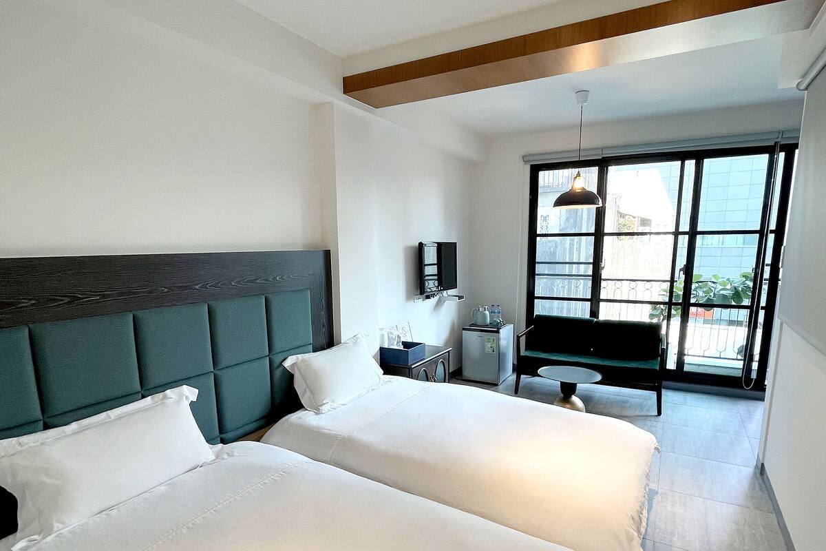 Ein Hotelzimmer mit zwei Betten, einem kleinen Schreibtisch, einem Stuhl, einem Fernseher und einem Balkon mit Blick.