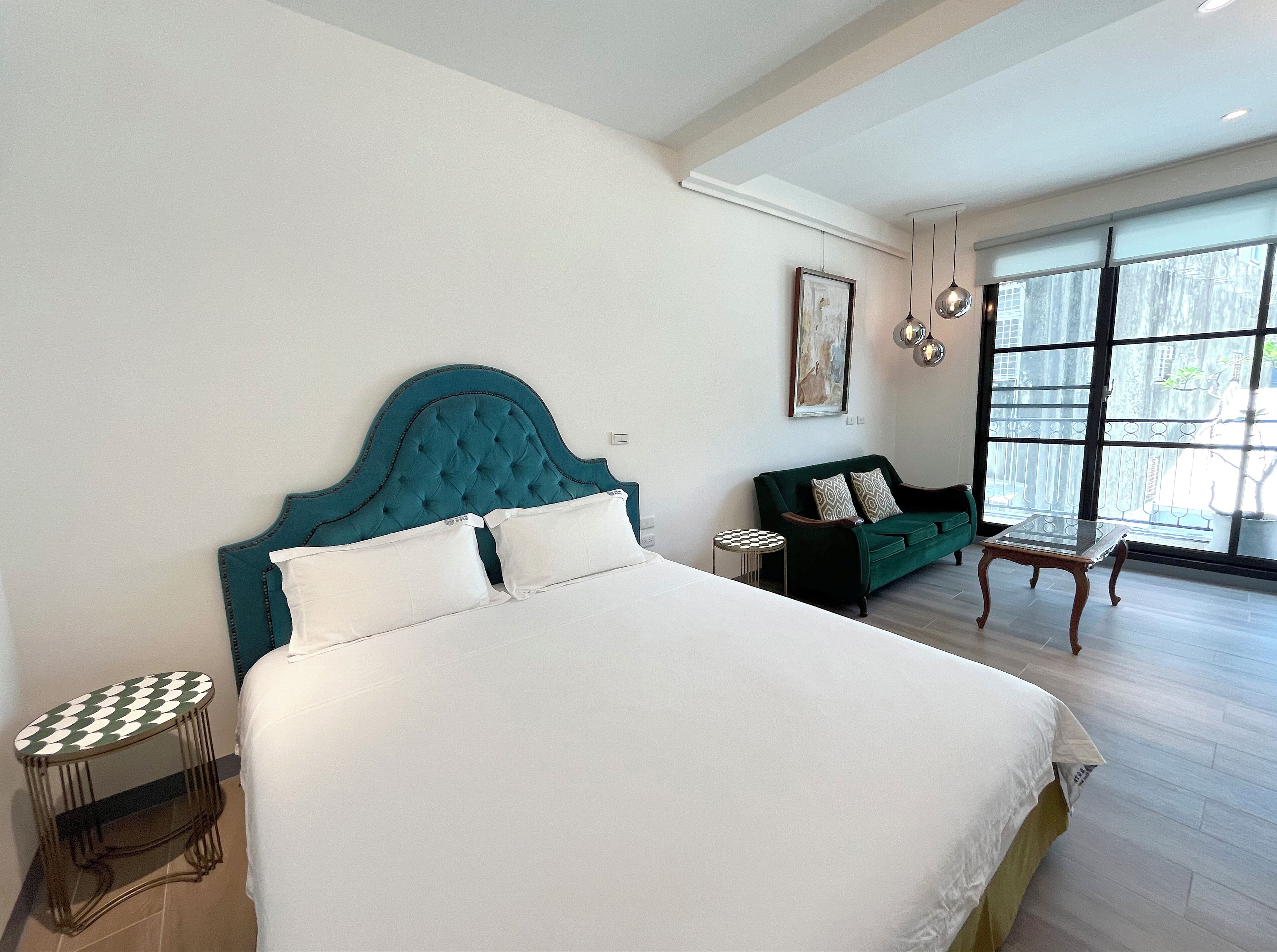 A hotel room with a large bed, a green sofa, a small table, and a large window with a view.