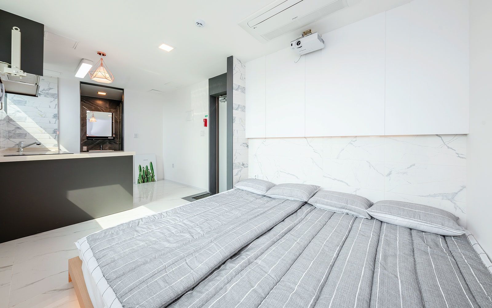 A modern hotel room with a large bed, a built-in desk, and a ceiling-mounted projector.