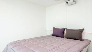 Ein Bett mit gesteppter Bettdecke und zwei Kissen, ein an der Decke befestigter Projektor und eine weiße Wand.