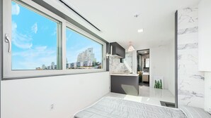 A modern bedroom with a large window, a bed, and a view of the cityscape. - I Stayed Pension Yeosu (Yeosu)