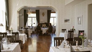 A dining area with multiple tables set for guests, featuring chandeliers and framed artwork on the walls. - Björkudden Hotell & Restaurang (Sandoverken)