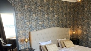 A bedroom with a large bed, a nightstand with a lamp, and a chair. - Björkudden Hotell & Restaurang (Sandoverken)