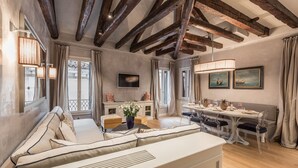 Un salón amplio con techo alto, vigas de madera a la vista, un sofá grande, una mesa de comedor con sillas y un televisor montado en la pared.