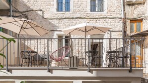 Un edificio con fachada de piedra, varias ventanas y terraza al aire libre con sillas y mesas.