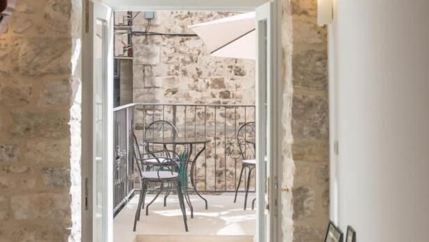 Una escalera conduce a un balcón con pared de piedra y barandilla de metal.