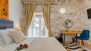 Un dormitorio con una cama, un escritorio, una silla, un espejo y una pared de piedra.