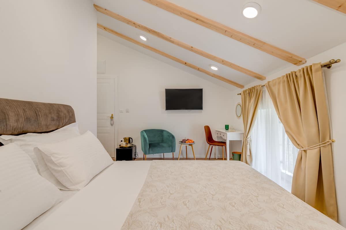 A bedroom with a bed, a desk, a chair, a television, and a window with curtains.