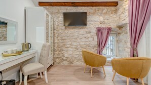 Una habitación con pared de piedra, vigas de madera, televisor de pantalla plana, escritorio con silla y dos sillas amarillas.