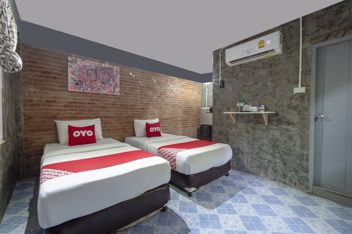 A hotel room with two beds, a brick wall, an air conditioning unit, and a tiled floor.