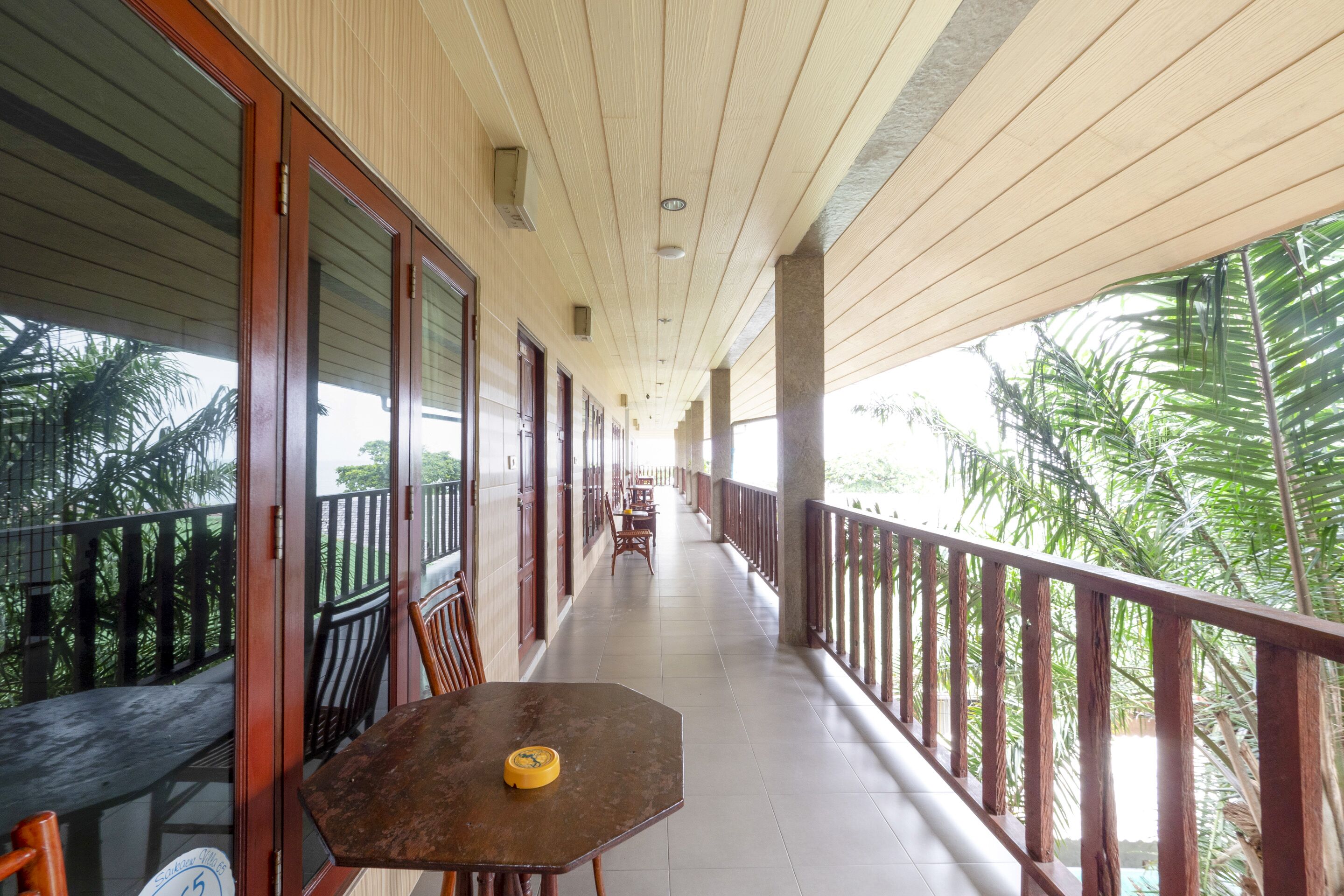 A covered corridor with wooden railings, a table with a yellow object, and a view of palm trees.