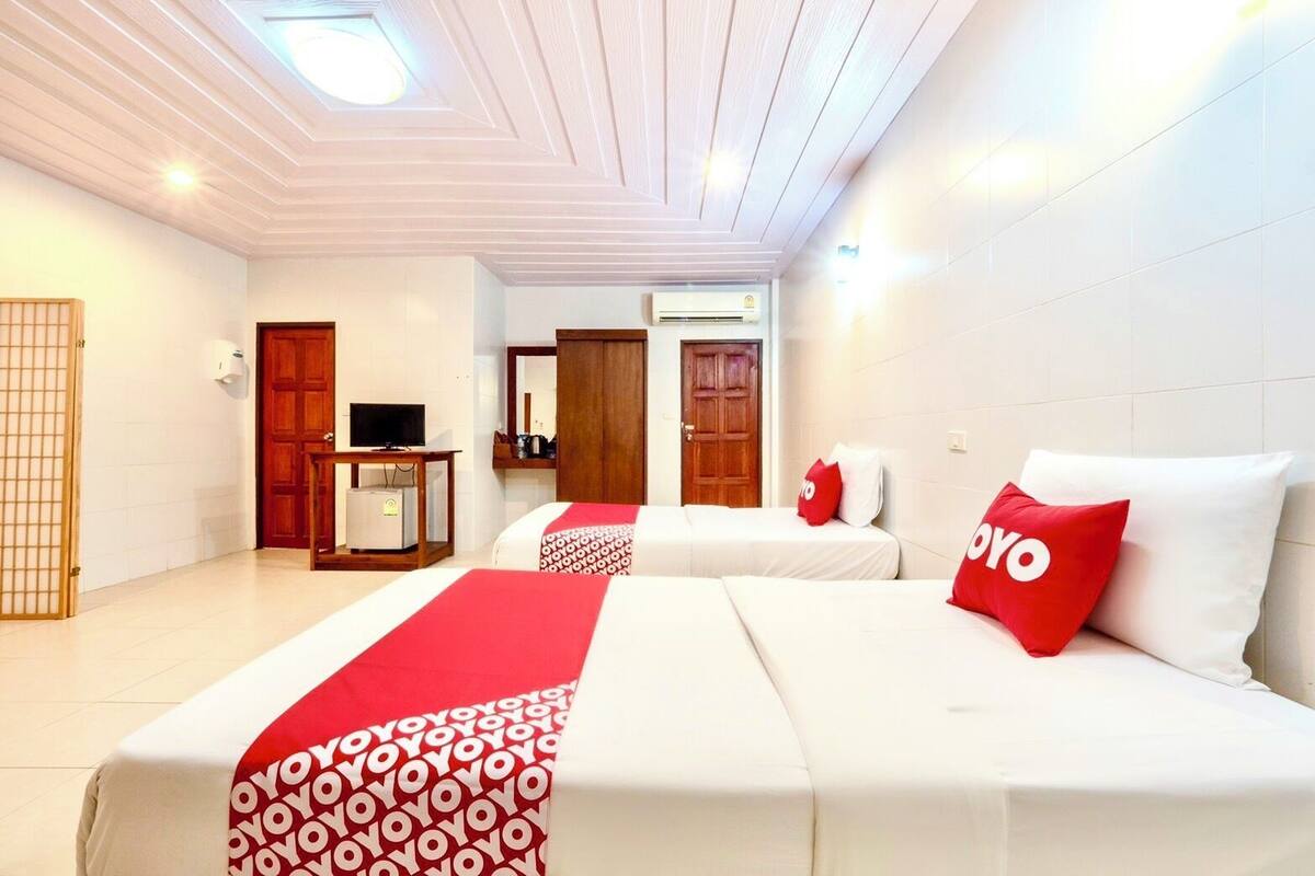 A hotel room with two beds, a TV, a desk, and an air conditioning unit.
