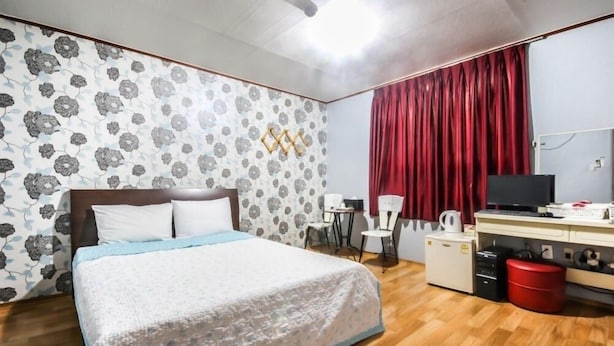 A bedroom with a bed, a desk with a computer, a TV, and a red curtain. - Royal Motel (Gwangju)