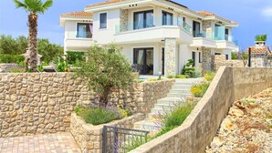 Uma casa moderna de dois andares com um muro de pedra de contenção, um pequeno jardim com lavanda e um céu azul límpido.