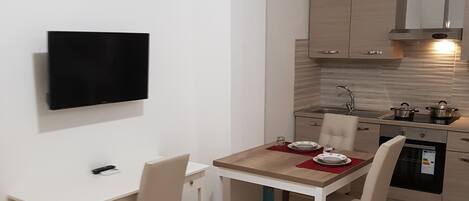 Una cocina compacta con comedor, un televisor de pantalla plana en la pared y un refrigerador pequeño.