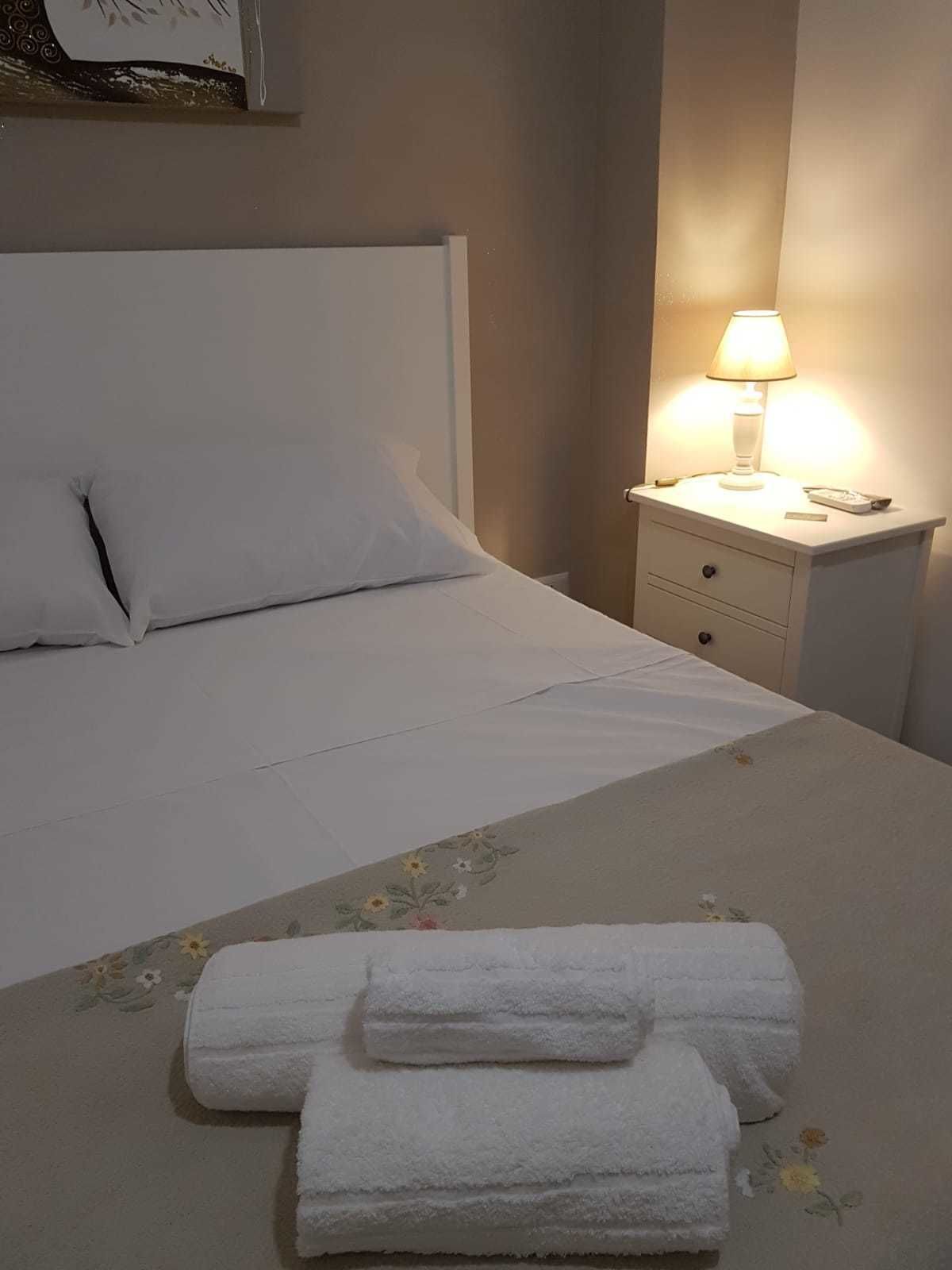 A neatly made bed with white linens and two rolled towels on the bed.