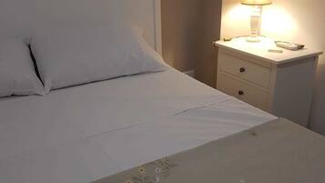 A neatly made bed with white linens and two rolled towels on the bed.