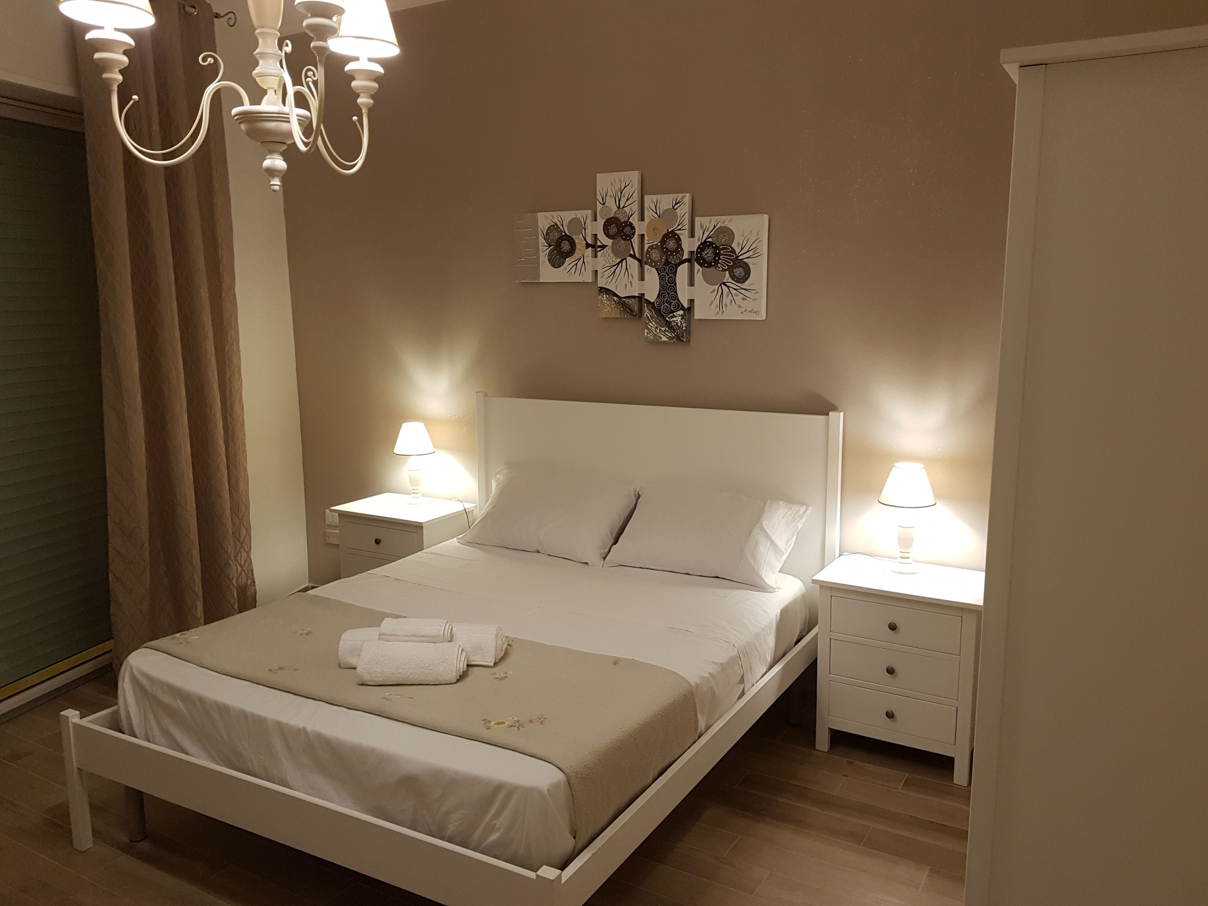 A neatly arranged bedroom with a bed, two bedside tables with lamps, a chandelier, and wall art.
