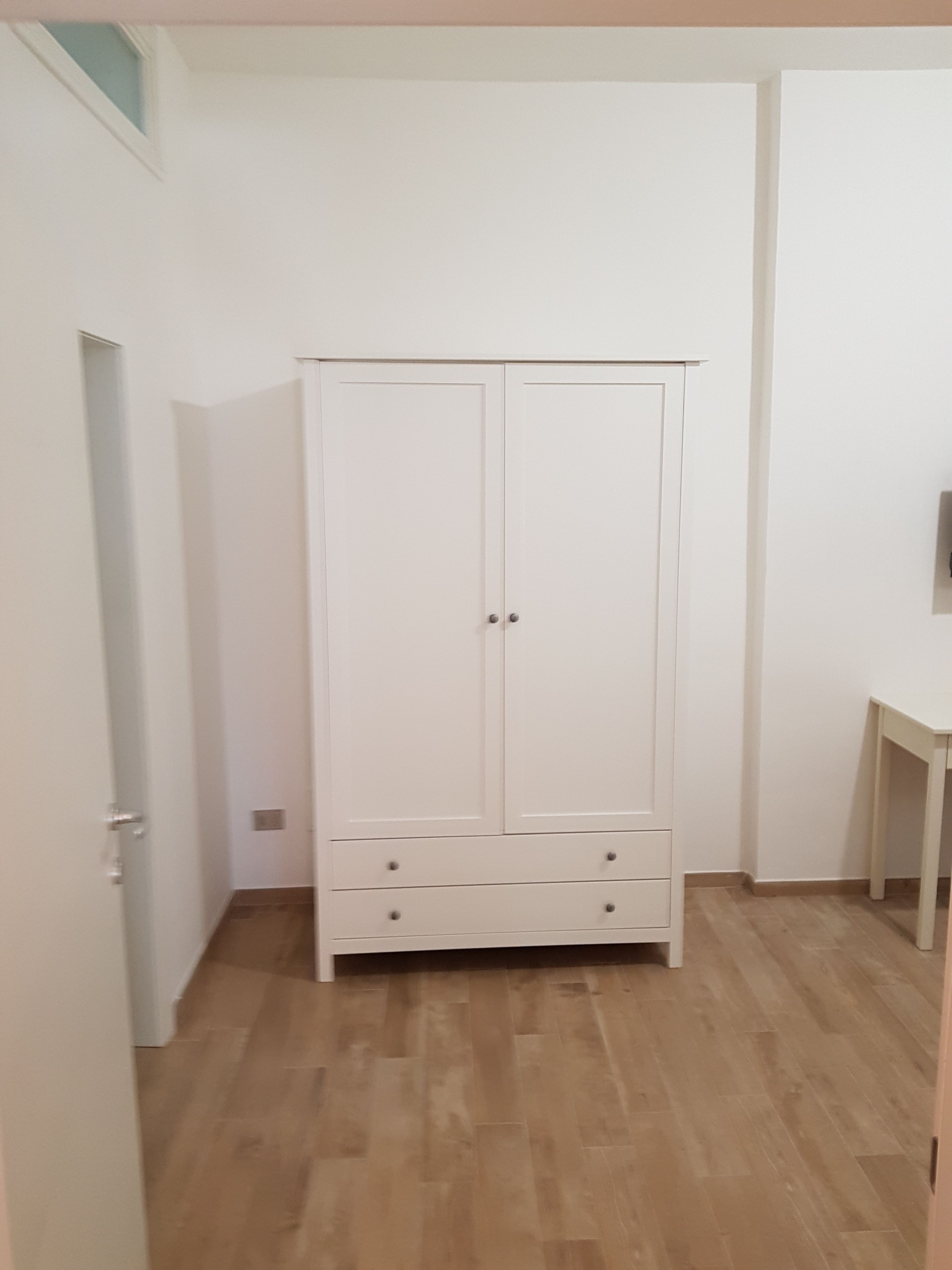 A room with a white wardrobe, a wooden floor, and a small table.