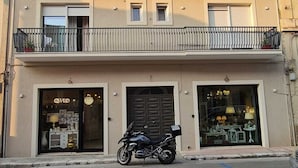Un edificio a due piani con un balcone al piano superiore, una motocicletta parcheggiata davanti e vetrine che espongono articoli.
