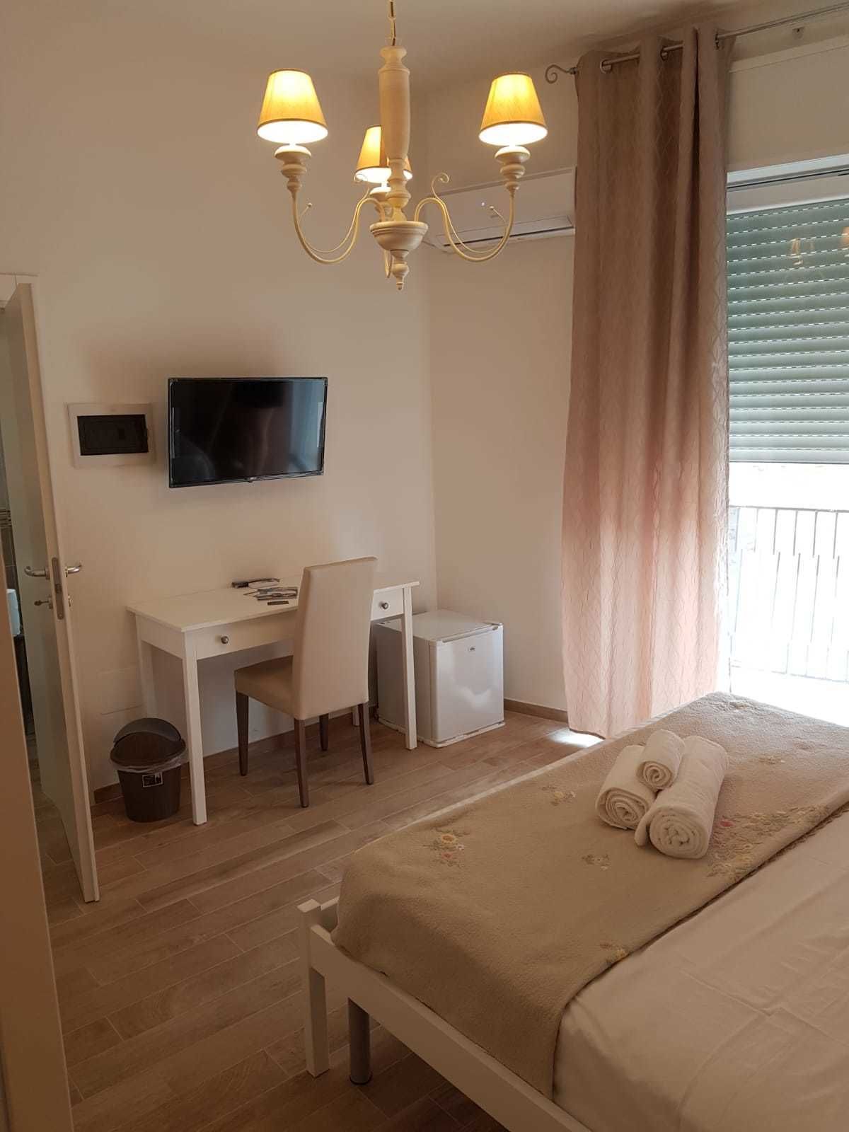 A hotel room with a bed, a desk with a chair, a television, and a small refrigerator.