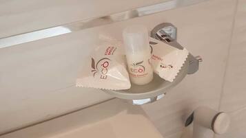 A bathroom with a white sink, a mirror, and toiletries on a shelf including a bottle of shampoo and a bar of soap.