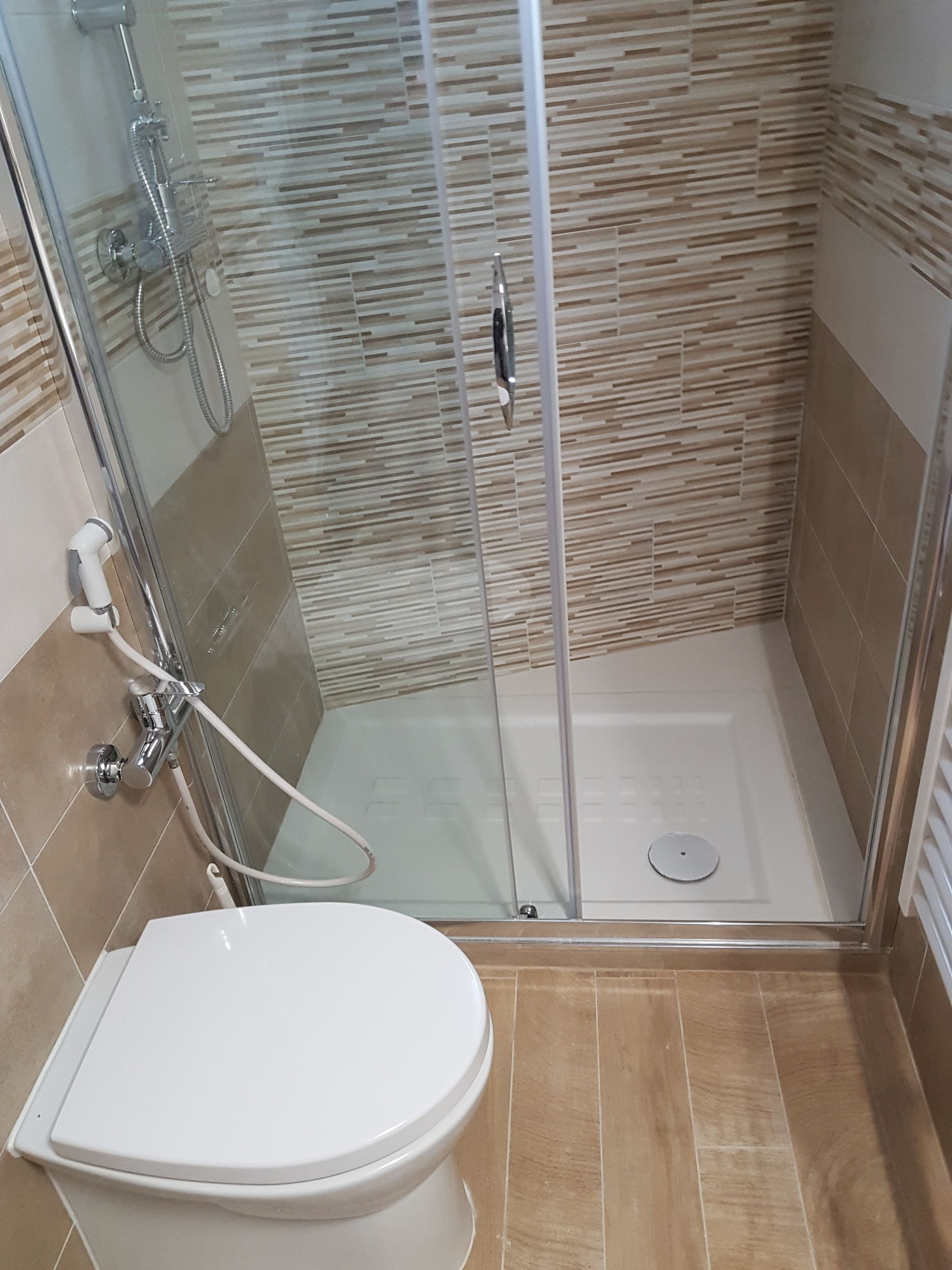 A bathroom with a glass-enclosed shower, a white toilet, and tiled walls.