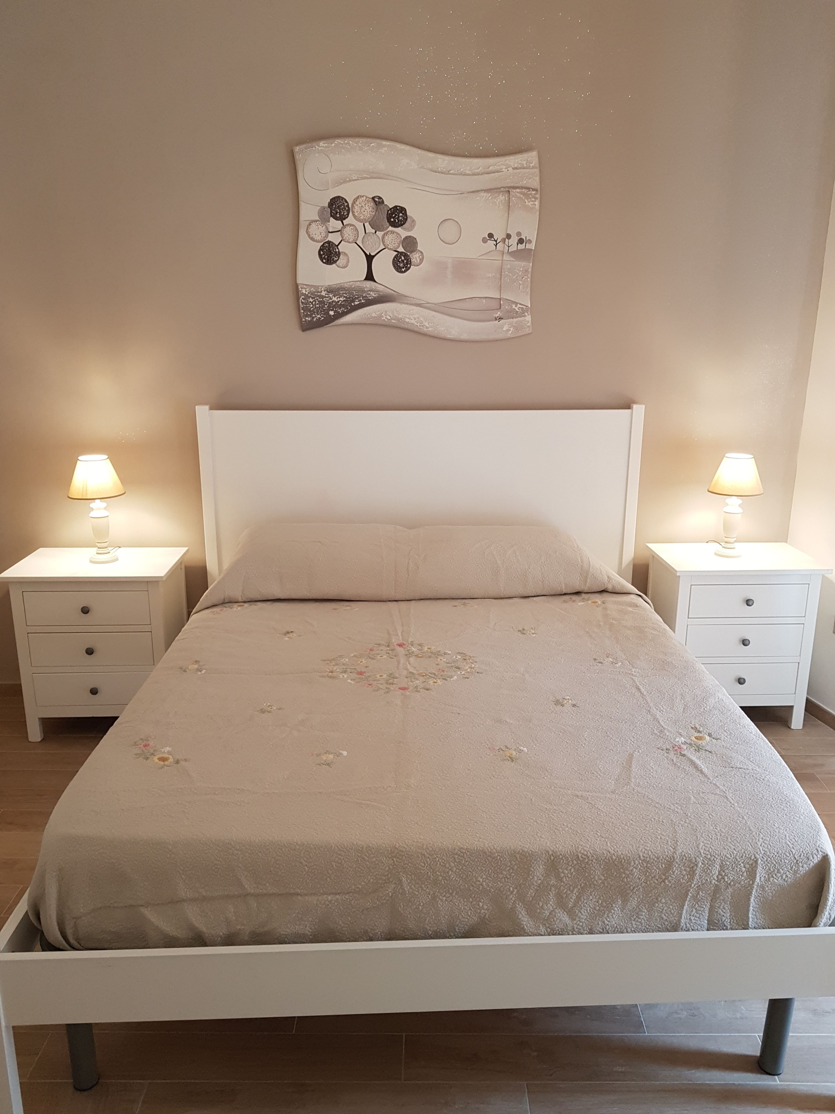 A bedroom with a bed, two bedside tables, and a wall-mounted artwork.