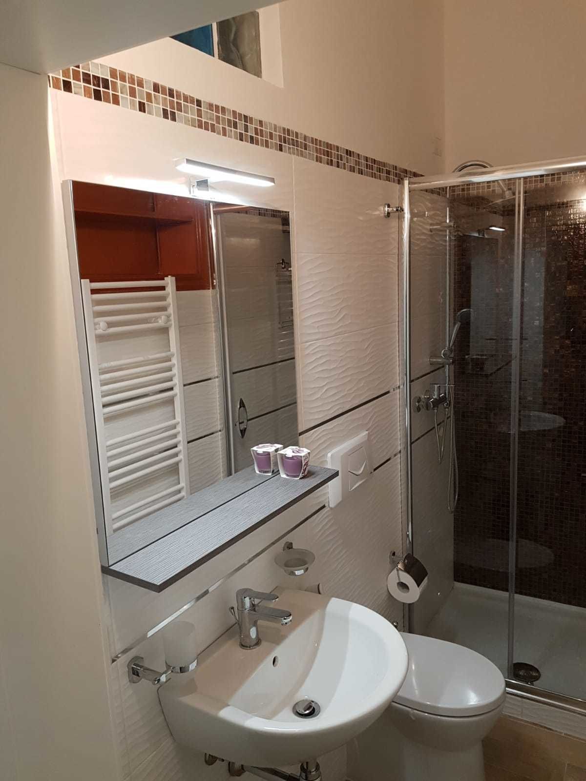 Une salle de bain avec un lavabo blanc, des toilettes, une douche en verre et un miroir avec une étagère.