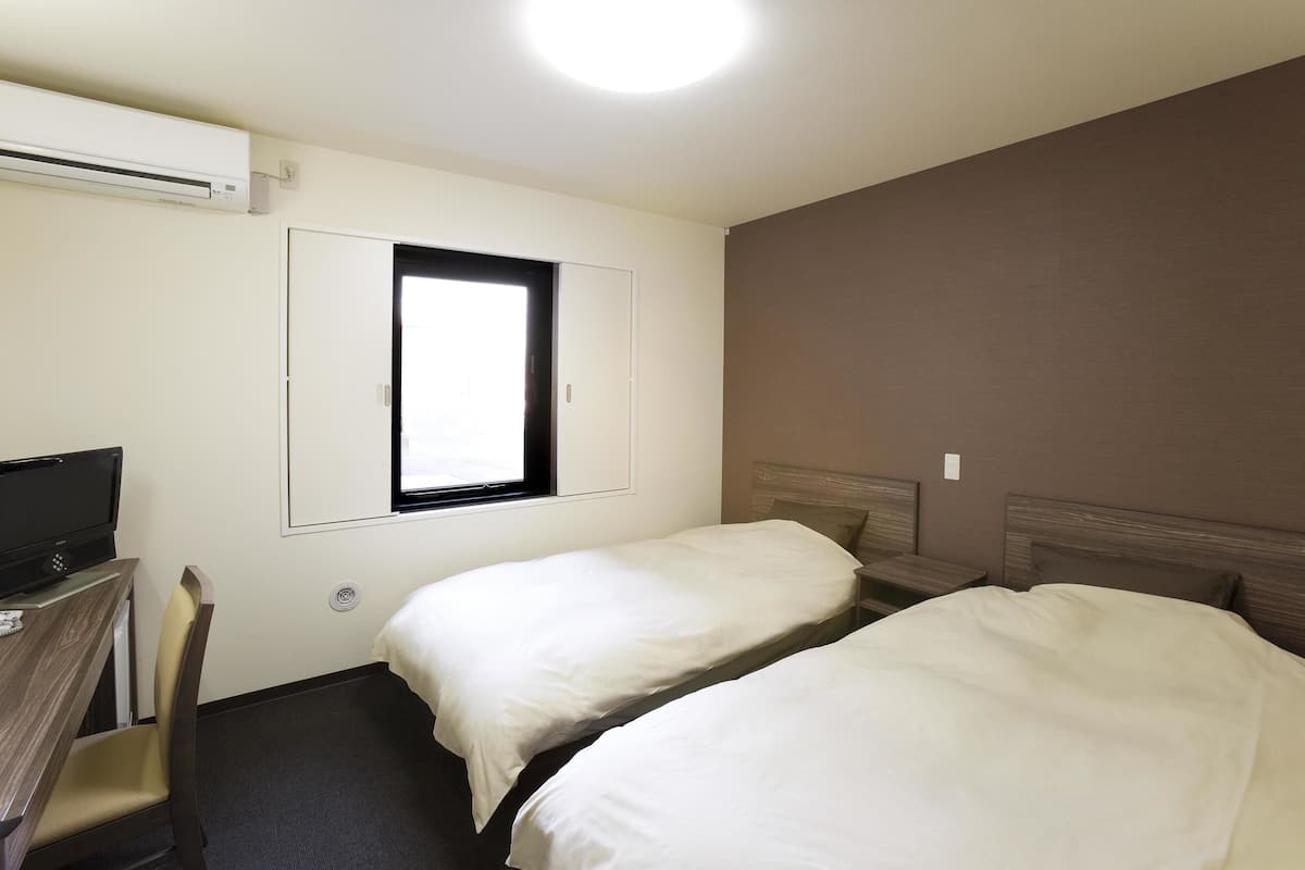 A room with two single beds, a desk with a chair, a television, and a window.