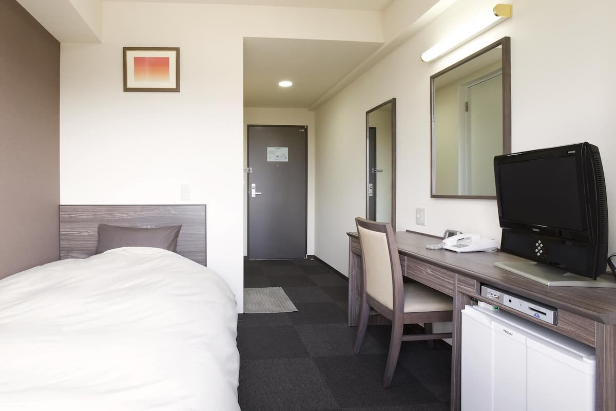 A hotel room with a bed, a desk with a computer, a chair, a television, and a mirror.