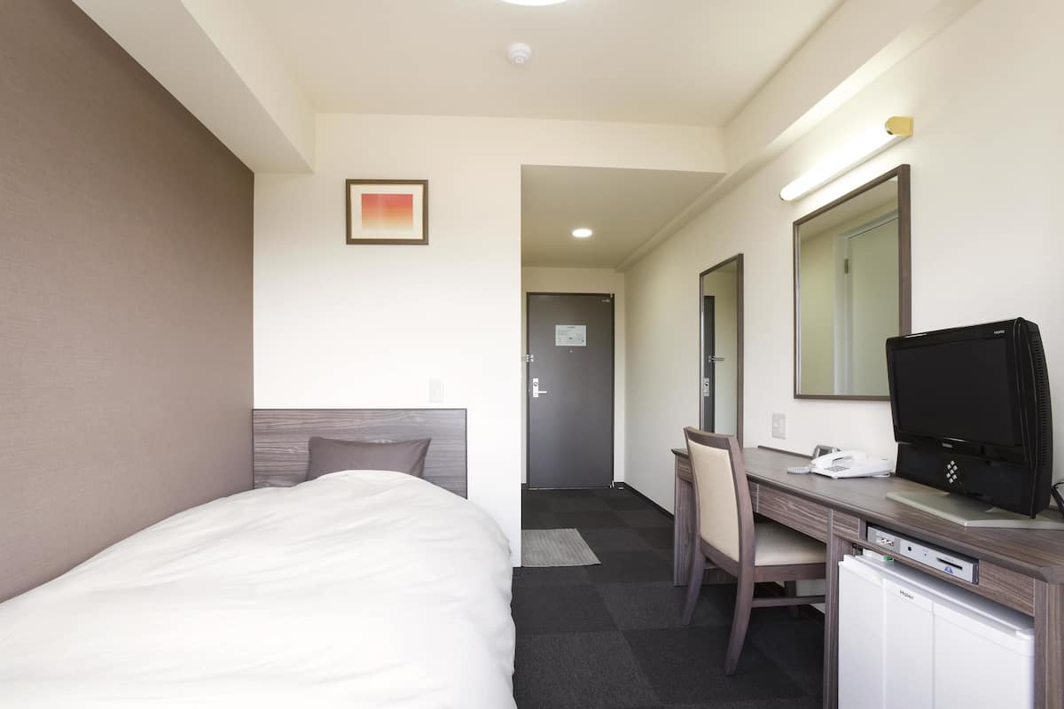 A hotel room with a bed, desk, chair, television, and a small refrigerator.