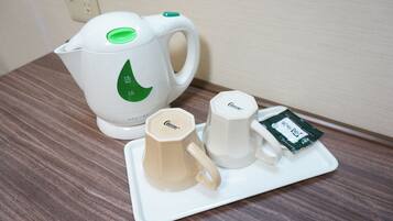 Een witte elektrische waterkoker met een groen logo, twee witte bekers en een dienblad met een theezakje op een houten tafel.