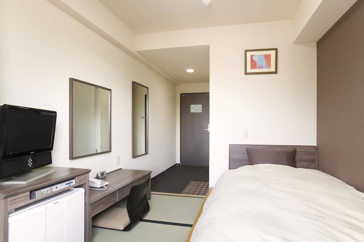 A hotel room with a bed, a desk with a computer and phone, a television, and a mirror.