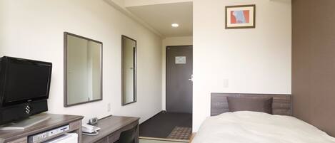 Una habitación de hotel con una cama, un escritorio con computadora y teléfono, una televisión y un espejo.