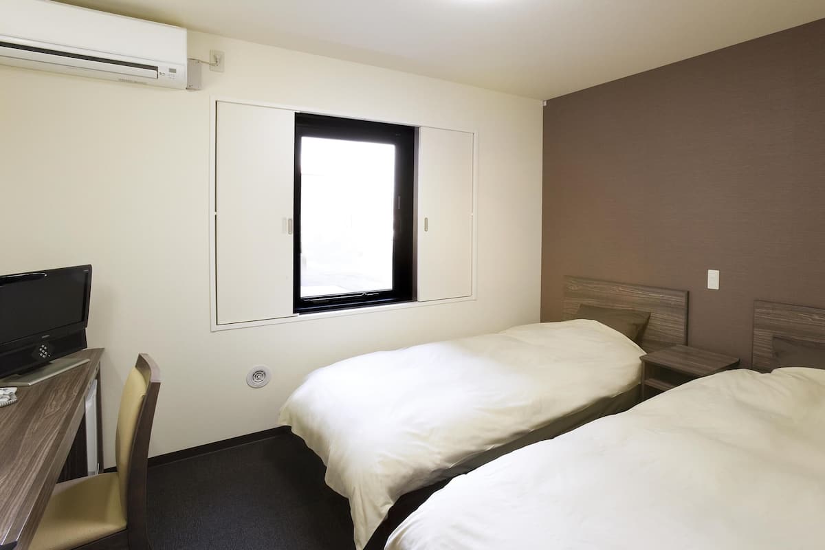 A hotel room with two beds, a TV, a window, and an air conditioning unit.