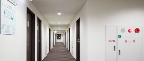 Pasillo de hotel con puertas numeradas del 501 al 520, un panel de alarma contra incendios y señales de salida de emergencia.