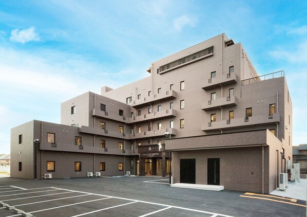 A modern hotel with a multi-story structure, a parking lot, and air conditioning units. - The Kato Hotel (Tokai)