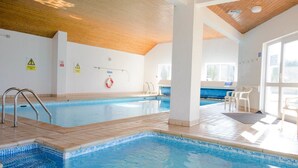Una piscina interior con agua cristalina, suelo de baldosas y señales de seguridad en las paredes.